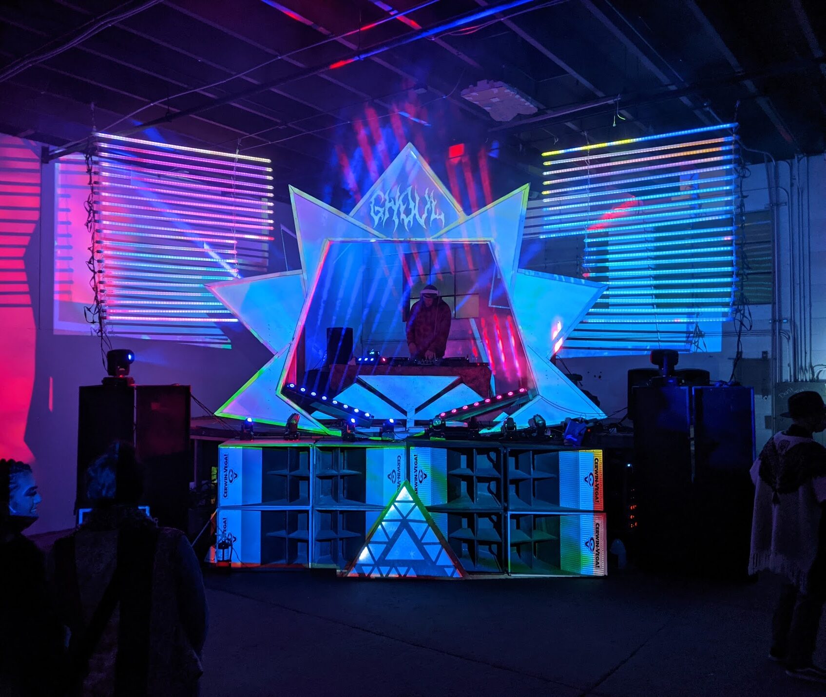 Projection-mapped DJ booth and winged stage props at a Sequence Sound System warehouse show
