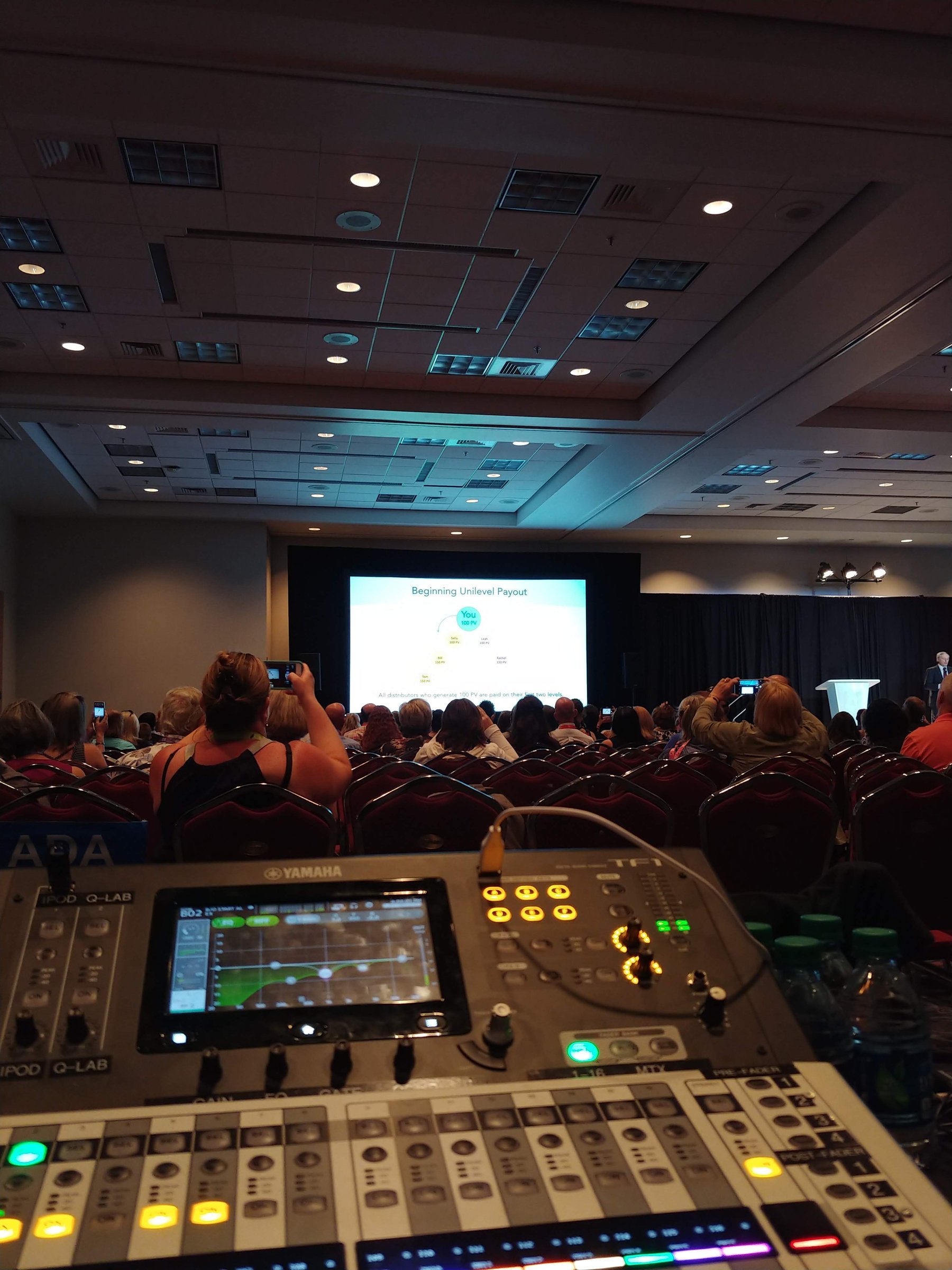 Yamaha TF1 audio console at the mix position with a corporate presentation and audience in the background