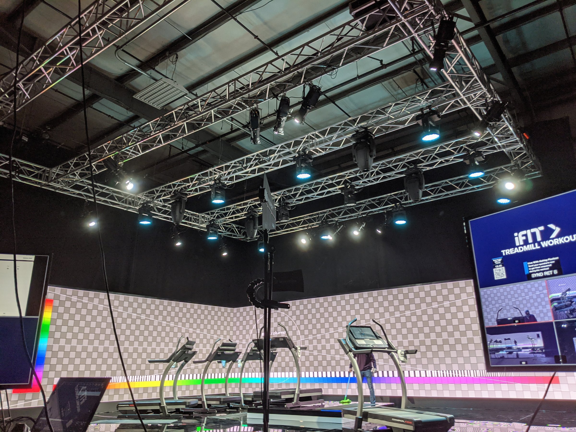 iFit broadcast studio with a lighting truss grid, treadmills on set, and an iFit workout graphic on the LED wall