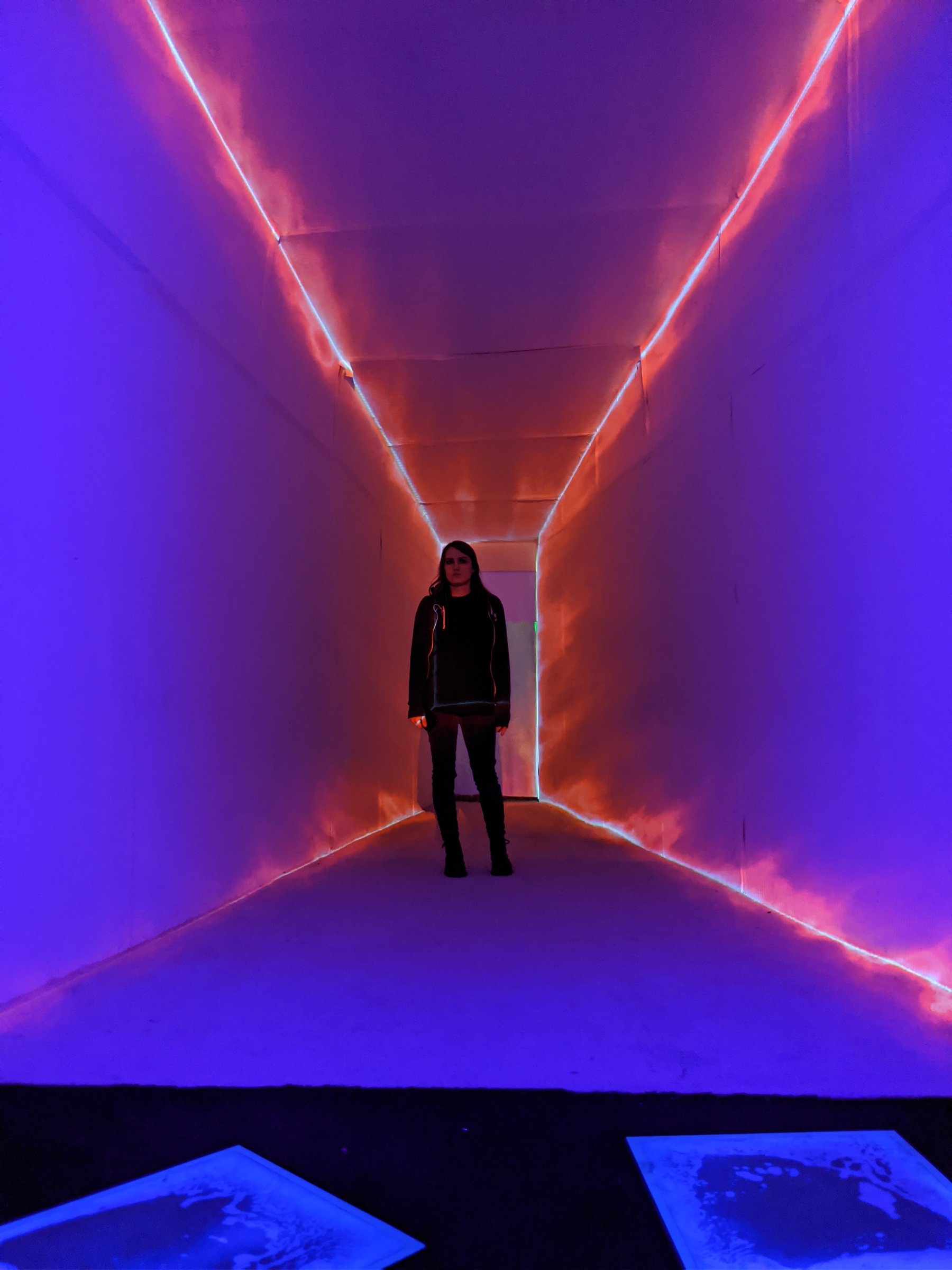 Person standing in a projection-mapped immersive light tunnel washed purple and orange at Dreamscapes