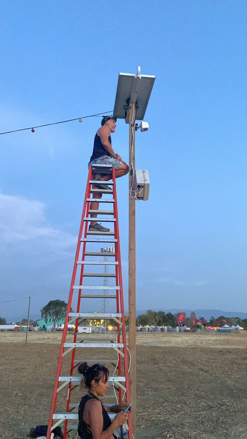 Technician on a ladder installing a pole-top access point at dusk